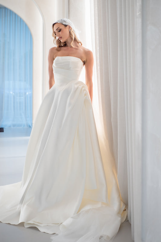 Woman in a strapless white wedding dress standing in front of a curtain