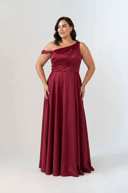 A woman modeling a floor-length, one-shoulder formal dress in deep burgundy with a draped bodice and flowing skirt, photographed against a light gray studio background.
