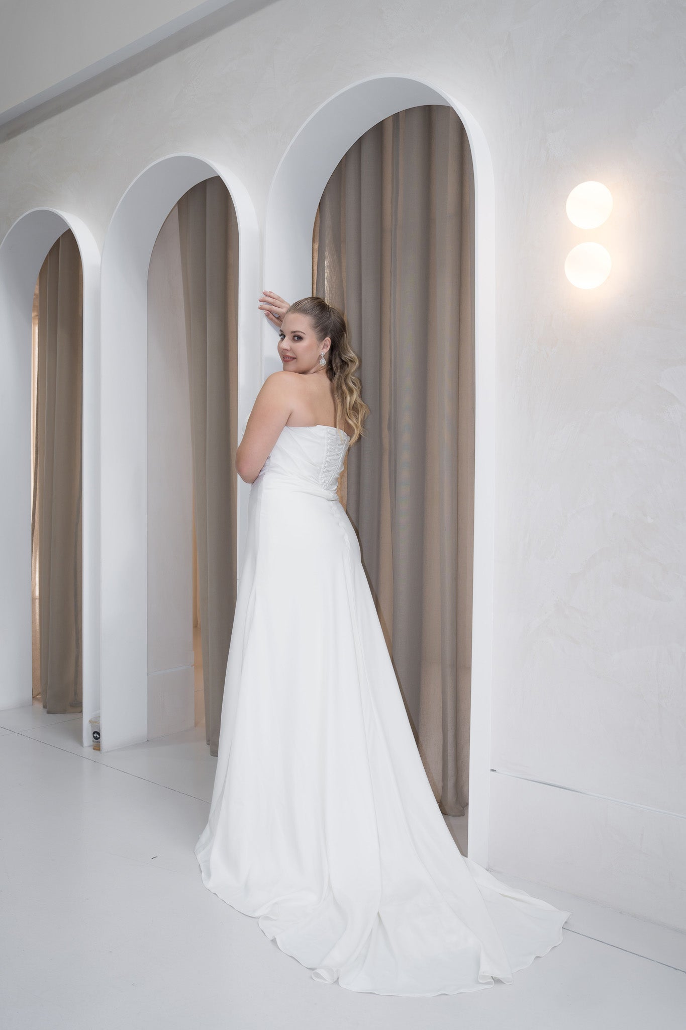 Woman in a white wedding dress standing in a modern architectural setting with arched doorways.
