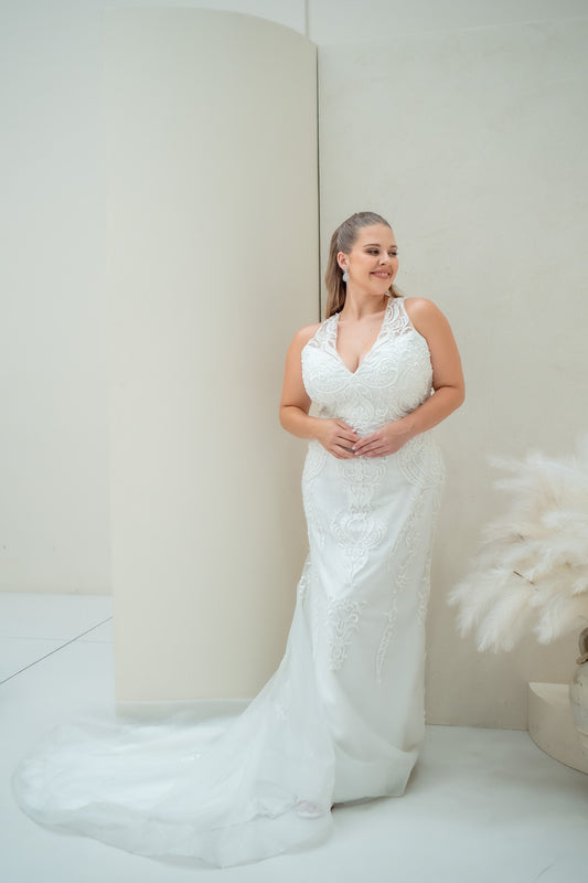 Woman in a white lace wedding dress standing against a plain background