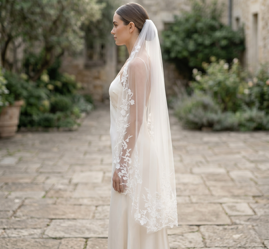 Woman wearing a white lace wedding dress and veil in an outdoor setting.