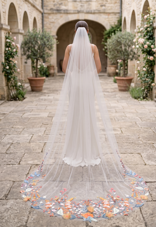 Person wearing a long wedding veil with colorful accents in an outdoor setting.