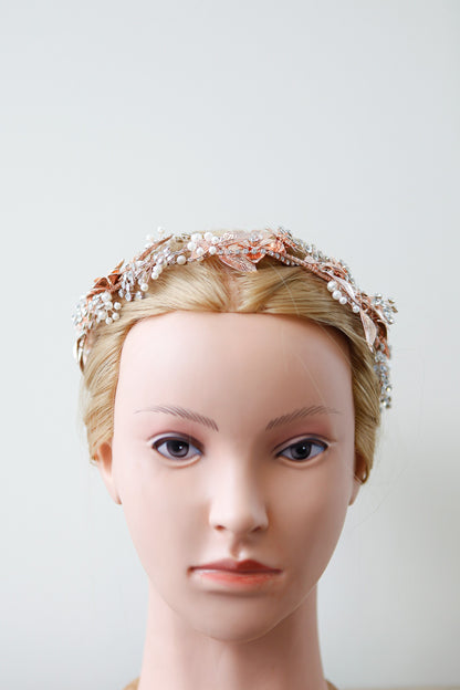 Mannequin head wearing a decorative headband with pearls and flowers on a plain background