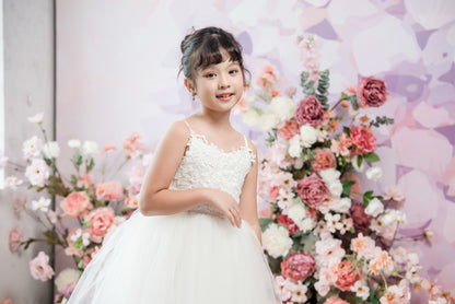 Young girl in a white dress standing in front of floral decorations