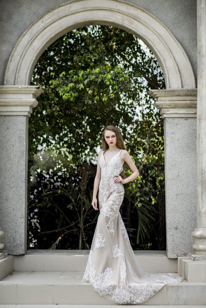 Woman in a white lace dress standing in front of an archway with greenery.