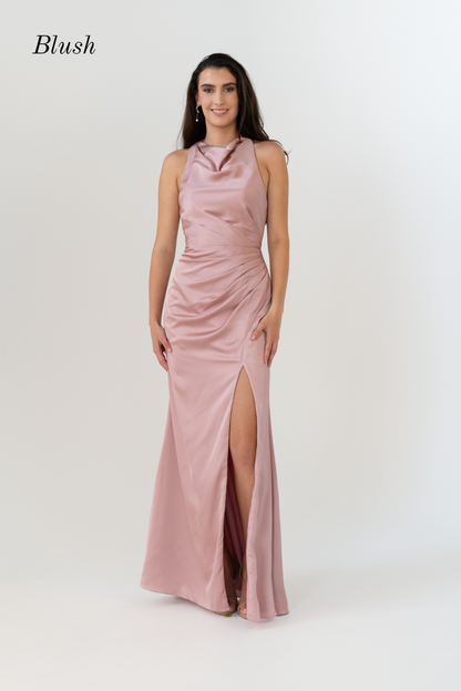 A woman modeling a sleeveless blush pink satin maxi dress with a high slit and draped neckline, set against a plain light gray studio background. The word 'Blush' is printed in the upper left corner.