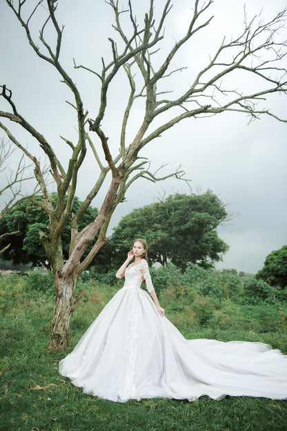 Bride in lace ball gown standing by tree in garden setting