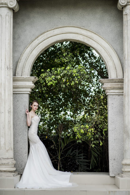 Woman in a white dress standing in front of a stone archway with greenery.
