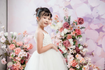 Young girl in a white dress standing in front of a floral backdrop