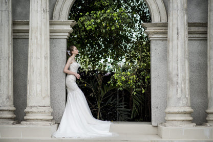 Woman in a white wedding dress standing in front of classical architecture with greenery.