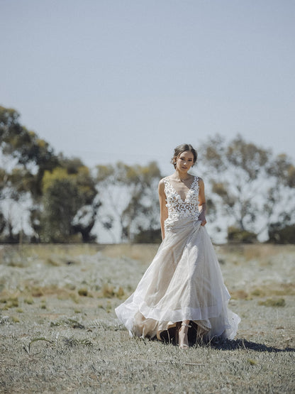 Woman in a white wedding dress standing in a field with trees in the background