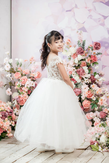 Young girl in a white dress standing in front of a floral arrangement with a soft pink background