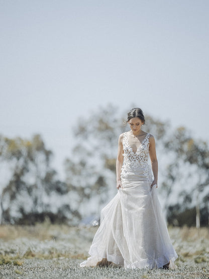 Woman in a white wedding dress standing in a field with trees in the background