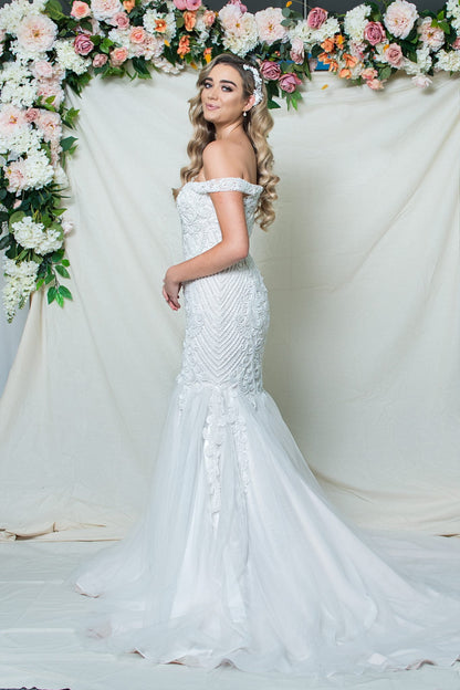 Woman in a white wedding dress standing in front of floral decorations.