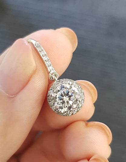 Diamond earring held between fingers against a dark background