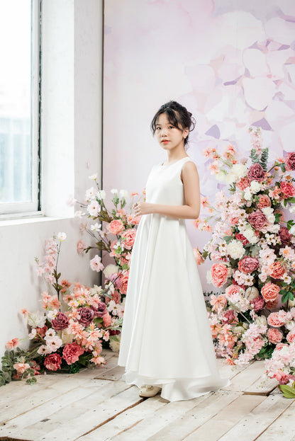 Woman in a white dress standing in front of a floral arrangement indoors.
