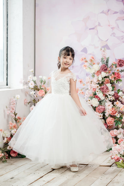 Young girl in a white dress standing in front of a floral arrangement.
