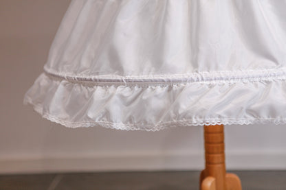 Close-up of a white petticoat with lace trim on a wooden hanger against a neutral background.