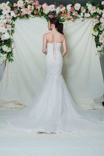 Woman in a white wedding dress standing in front of a floral archway.