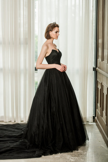 Woman wearing a black strapless gown standing in a room with white curtains.