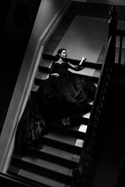 Woman in a dark dress standing on a staircase in a dimly lit room