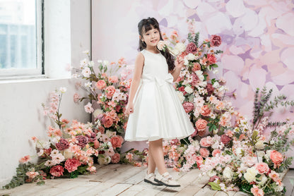 Young girl in a white dress standing among flowers with a floral backdrop