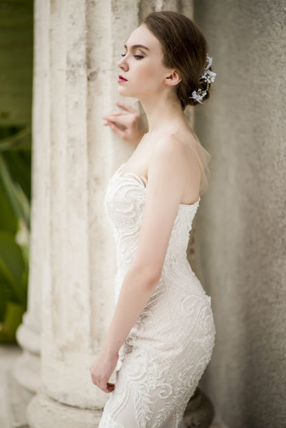 Woman in a white lace wedding dress standing against a classical column.