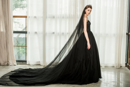 Woman in a black evening gown with a long train standing in a room with large windows