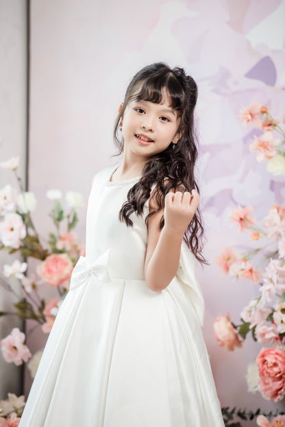 Young girl in a white dress standing in front of a floral backdrop