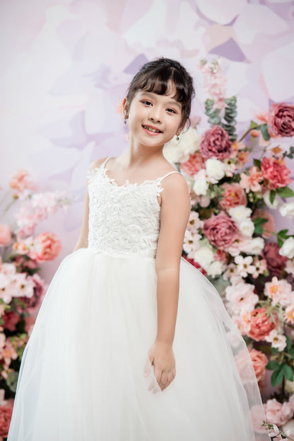 Young girl in a white dress standing in front of a floral backdrop