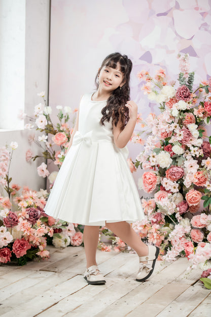 Young girl in a white dress standing in front of floral decorations