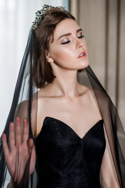 Woman wearing a black dress and veil with a neutral background
