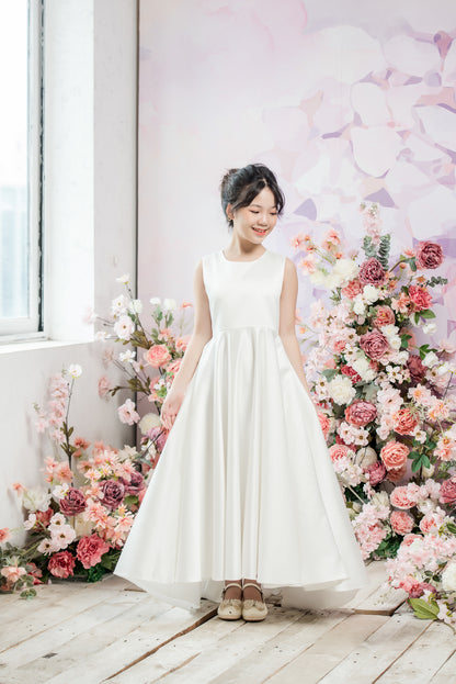 Woman in a white dress standing in front of a floral arrangement indoors.