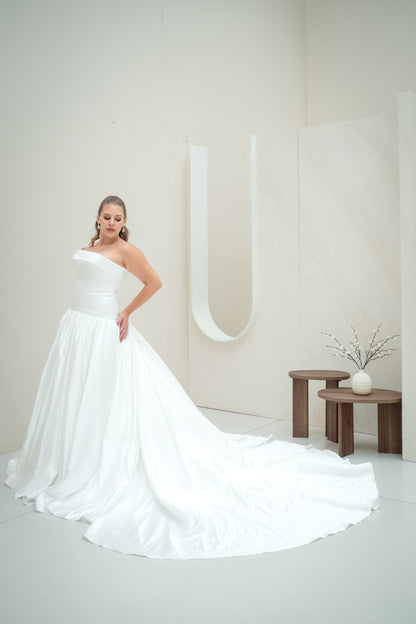 Woman in a white wedding dress standing in a minimalistic room with a large letter 'U'