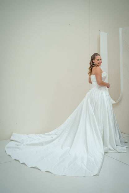 Woman in a white wedding dress with a long train against a plain background