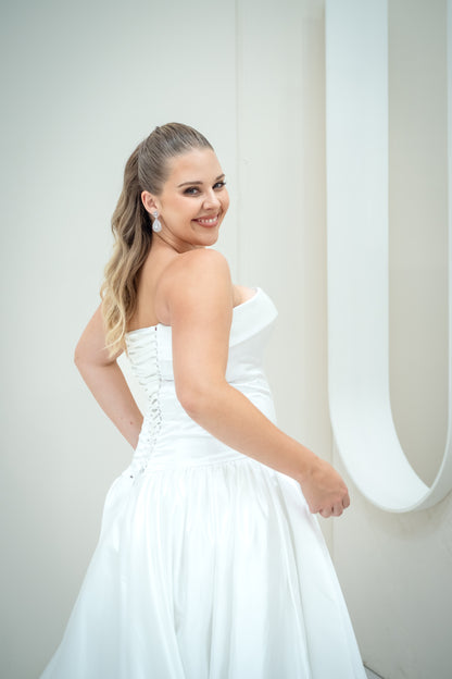Woman in a white strapless dress posing against a plain background