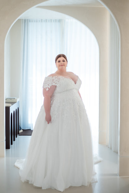 Woman in a white wedding dress standing in a bright room with large windows