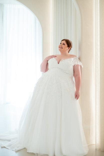 Woman in a white wedding dress standing in front of large windows with sheer curtains