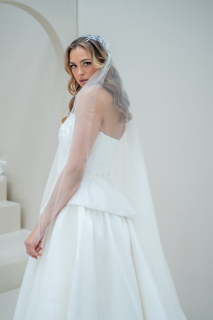 Woman in a white wedding dress with a veil standing against a plain background