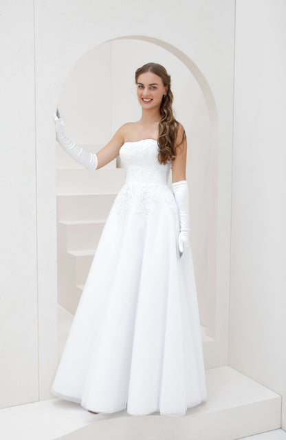 Woman in a white strapless gown with long gloves standing in a white room.