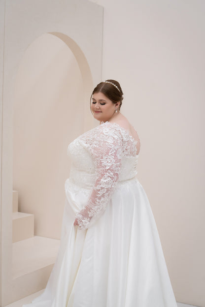 Woman in a white wedding dress with lace sleeves standing against a light-colored wall.