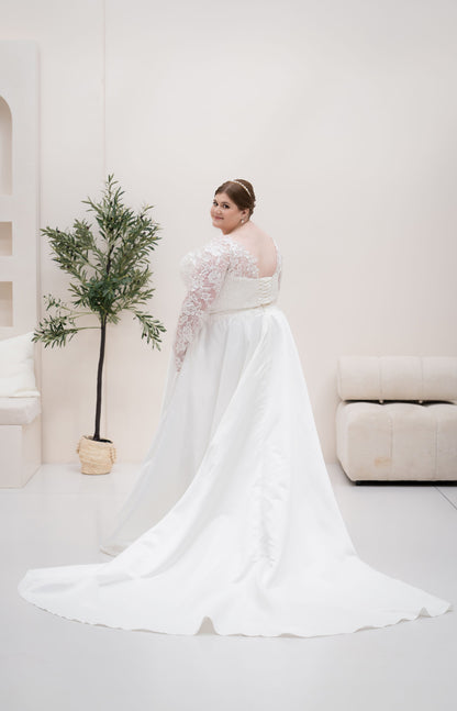 Woman in a white wedding dress standing in a minimalistic room with a plant.
