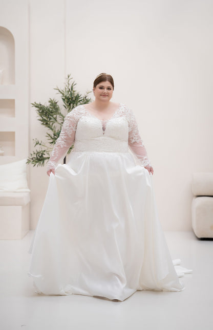 Woman wearing a white wedding dress with lace sleeves in a bright room.
