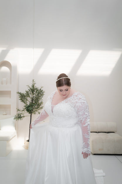 Woman in a white wedding dress with lace sleeves standing in a bright room.