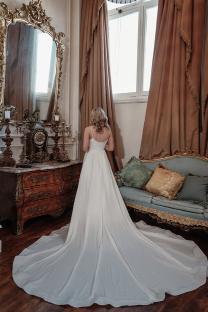 Woman in a white wedding dress standing in a room with ornate furniture and large mirror