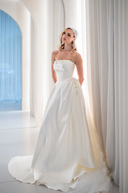Woman in a strapless white wedding dress standing in a bright, elegant interior setting
