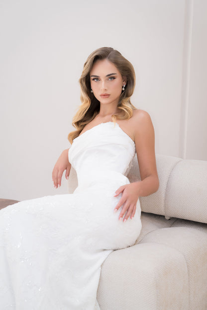 Woman in a white strapless dress sitting on a white couch against a white background