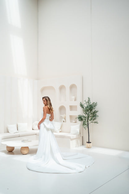 Woman in a white wedding dress standing in a minimalistic room with a white couch and plant