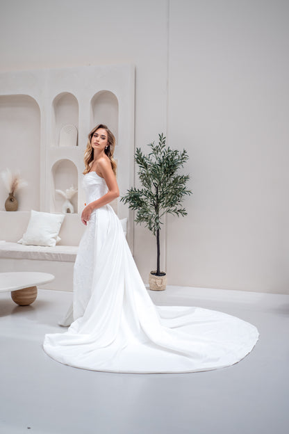 Woman in a white wedding dress standing in a modern, minimalistic room with a plant and bench