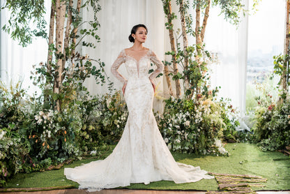 Woman in a white wedding dress standing in a decorated outdoor setting with flowers and greenery.